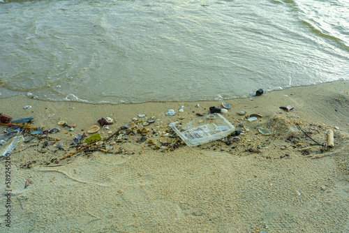 Plastic waste dumped on the beach by tourists eating and drinking along with seashells.