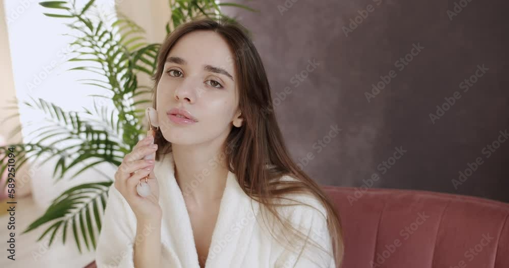 Beautiful woman with perfect smooth healthy skin is getting massage face using jade facial roller. Beauty treatment at home. A woman massage her skin with a dermatology tool. Morning beauty rituals. Beautiful woman with perfect smooth healthy skin is getting massage face using jade facial roller. Beauty treatment at home. A woman massage her skin with a dermatology tool. Morning beauty rituals.