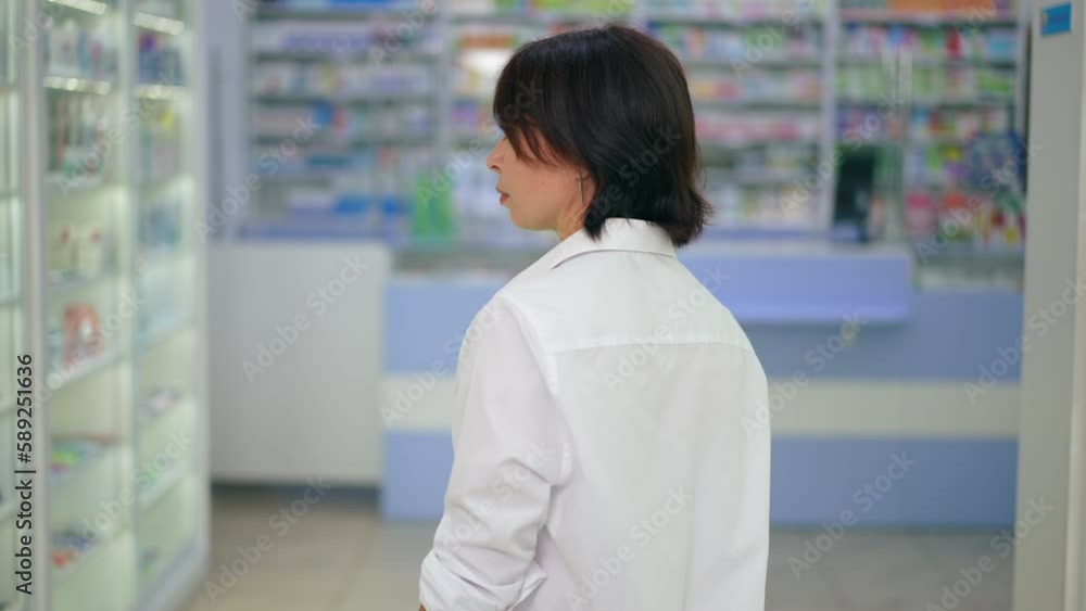 Back view Caucasian woman walking along rows of shelves in drugstore looking around. Tracking shot of thoughtful female customer choosing medications in pharmacy indoors. Slow motion Back view Caucasian woman walking along rows of shelves in drugstore looking around. Tracking shot of thoughtful female customer choosing medications in pharmacy indoors. Slow motion