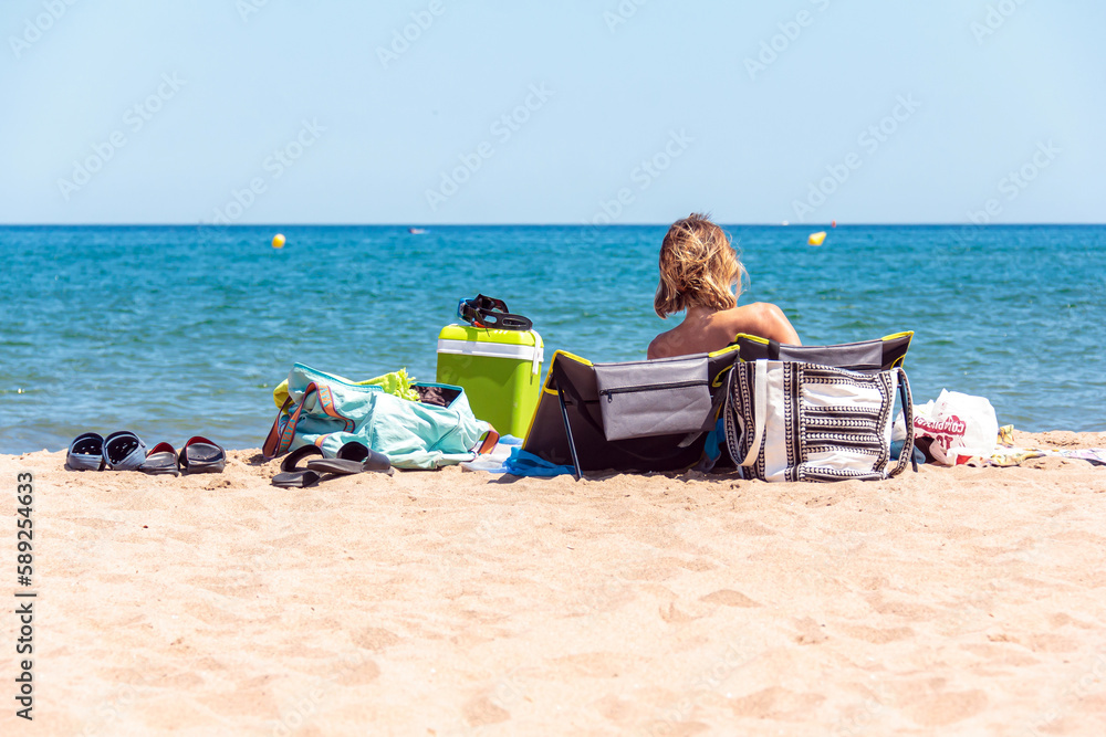 woman with relaxed back sitting on a beach chair in front of the sea 