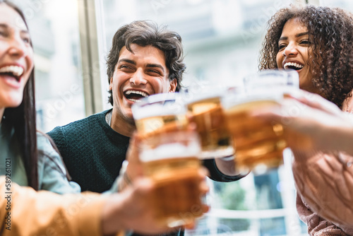 Multiracial friends drinking beer glasses sitting at brewery pub- Young group of happy people having fun toasting pint at bar enjoying happy hour time- Life style food and beverage concept with guys