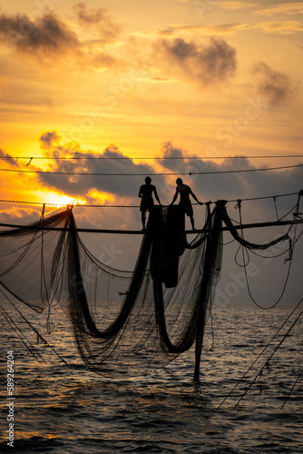 Silhouette of fishermen pulling a nets on fishing poles at sea in Tra Vinh province, Vietnam, Asia during sunrise, local people call it is Day hang khoi. photo