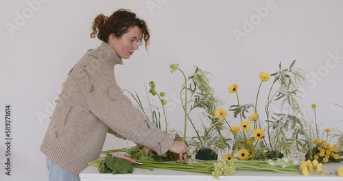 female doing new bouquet. Florist makes a floral oasis. Girl working in flower shop studio. Female florist artist cleans flowers for a beautiful bouquet, workplace view. High quality 4k footage