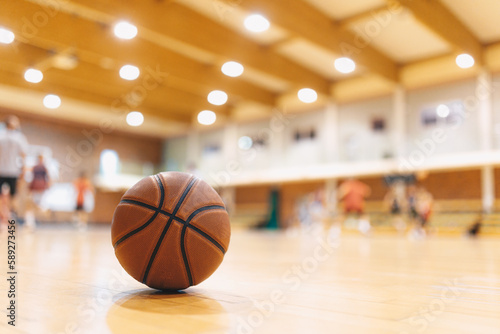 Classic Orange Basketball Ball On Wooden Sports Court. Junior Level Basketball Players Playing Game in Blurred Background. Basketball Training Background. © matimix