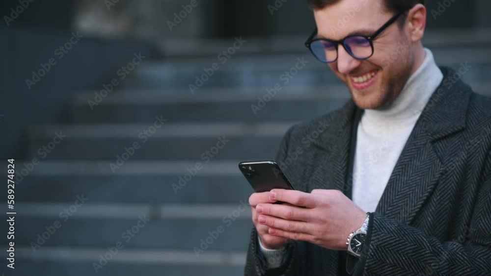 Texting and smiling. Man in black suit is outdoors with smartphone. Texting and smiling. Man in black suit is outdoors with smartphone.