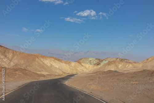 Panoramic view of endless empty road leading to colorful geology of multi hued Artist Palette rock formations in Death Valley National Park near Furnace Creek  California  USA. Black mountains
