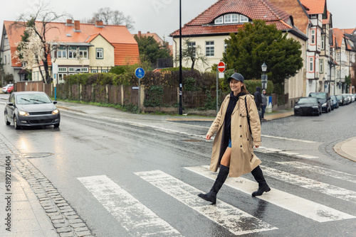 Obraz na płótnie Young adult trendy stylish beautiful caucasian happy smiling woman enjoy walking by road crosswalk in Europe rainy day