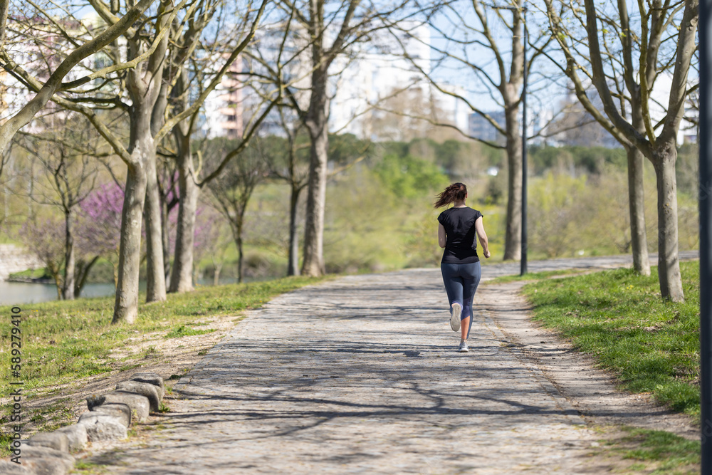 Adult woman jogging in the park - back view