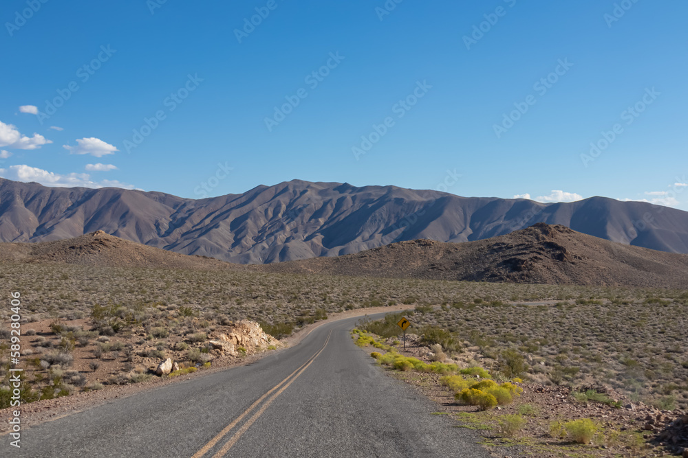 Endless road stretching straight through Death Valley National Park, California, USA. Highway in dry Mojave desert on sunny summer day with Amargosa Mountain Range in back. Freedom road trip concept