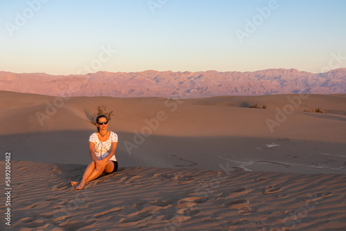 Touristic woman enjoying the sunrise with scenic view on Mesquite Flat Sand Dunes, Death Valley National Park, California, USA. Morning walk in Mojave desert with Amargosa Mountain Range in back. photo