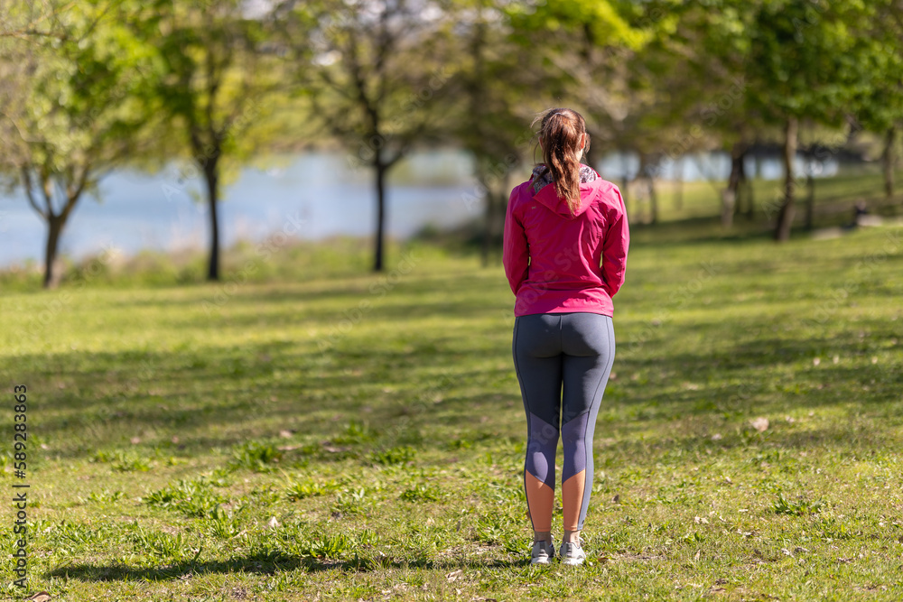 An adult woman in sports clothes standing on the field - view from the back