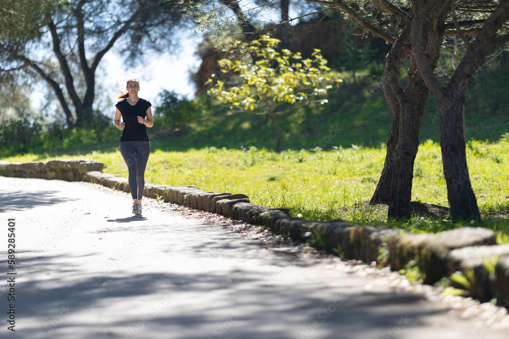 Fototapeta premium Fitness concept - an adult woman jogging in the green park