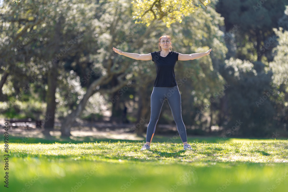 An adult smiling woman in sports doing fitness exercise in the park