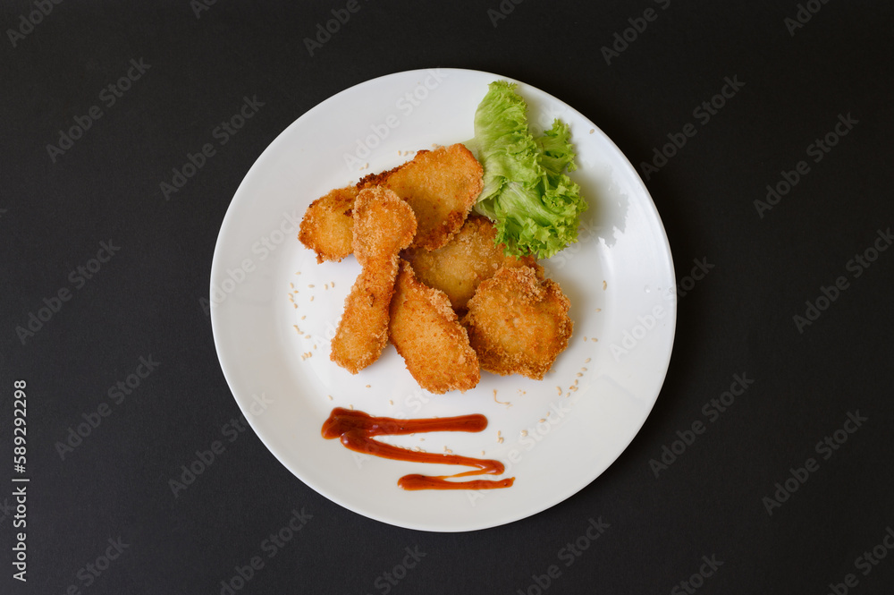 Chicken nuggets with sauce and lettuce on a plate, white plate and black background. Chicken nuggets with sauce and lettuce on a plate, white plate and black background.