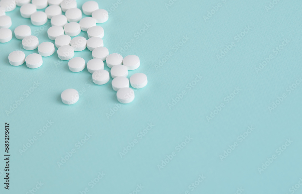 White pills are scattered on a light blue background. The tablets are located in the upper corner.