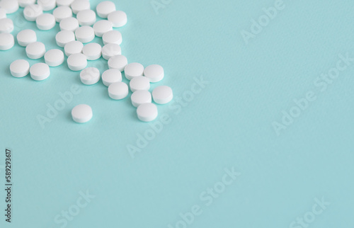 White pills are scattered on a light blue background. The tablets are located in the upper corner.