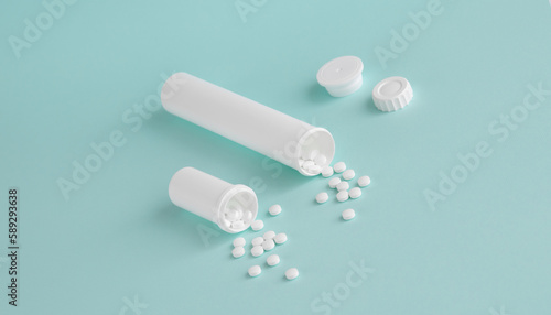 Two white medical bottles with white pills. Tablets are scattered on a light blue background, top view.