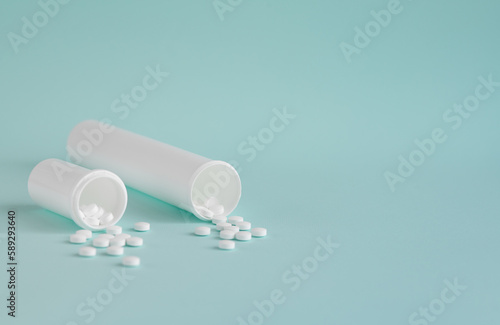 Two white medical bottles with white pills. Tablets are scattered on a light blue background.