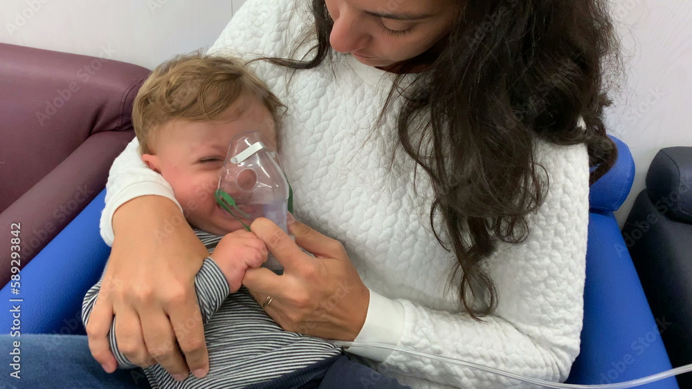 Mother giving respiratory inhaler to sick crying baby toddler Mother giving respiratory inhaler to sick crying baby toddler