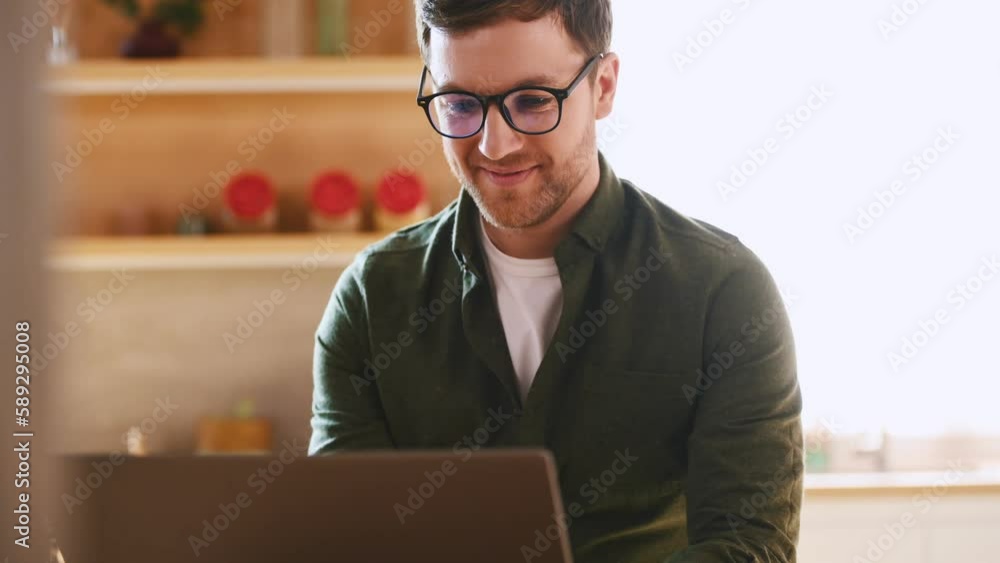 Cheerful man in glasses is sitting by laptop indoors. Cheerful man in glasses is sitting by laptop indoors.