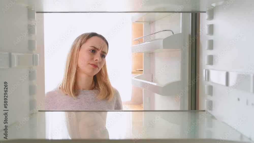 Woman opens the refrigerator door, it is empty inside, she is disappointed.