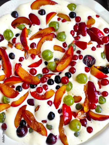 Plate of uncooked clafouti with berries and fruits. Close-up view from above. Homemade berry clafoutis pie