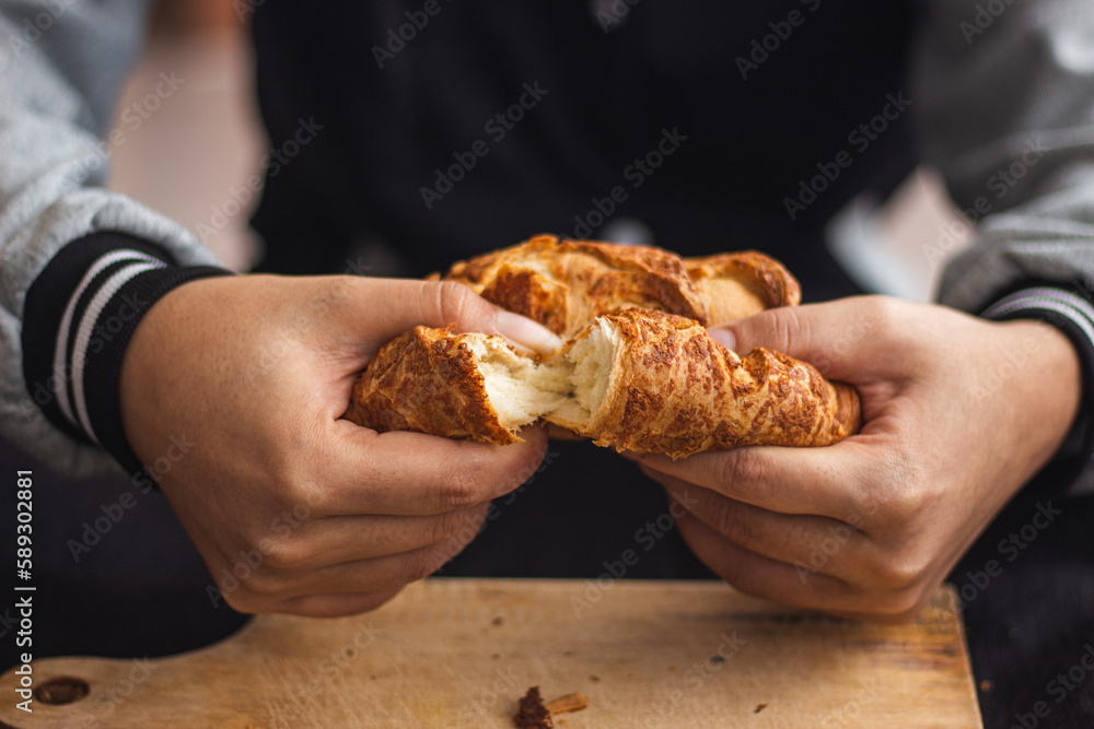 pan de cuajada partiéndose por la mitad por unas manos de una mujer.  hecho de manera casera 