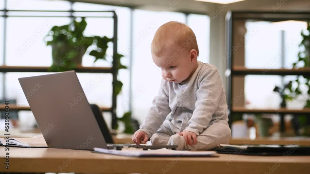 Cute baby boy is sitting on the table by laptop in the modern office. Cute baby boy is sitting on the table by laptop in the modern office.