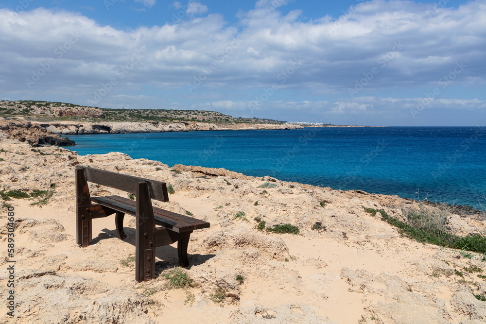 A wooden bench by the ocean. Sea with blue water and a rest bench on the shore