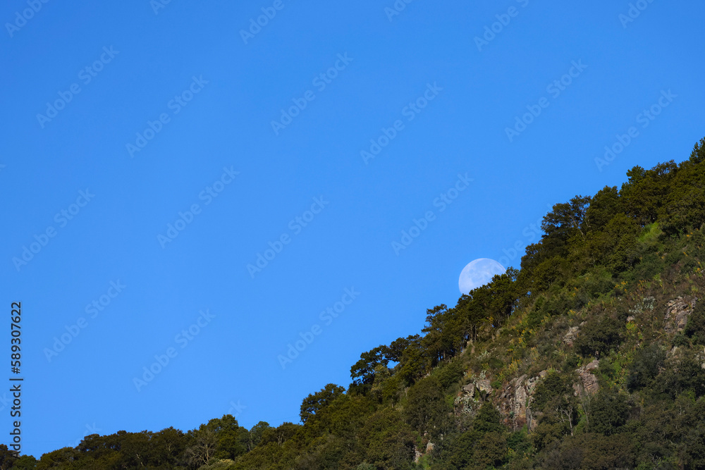 Moon behind mountain by day Moon behind mountain by day