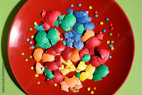 Broken Easter colourful eggshell pieces isolated on a red plate background. Easter treats. Flat lay,above. Abstraction