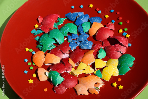 Broken Easter colourful eggshell pieces isolated on a red plate background. Easter treats. Flat lay,above. Abstraction