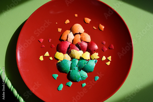 Pieces of colourful crushed easter eggshell folded in the shape of an egg Isolated on a red plate on a green background