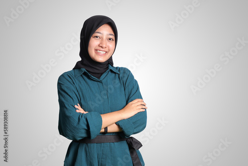 Portrait of cheerful Asian muslim woman with hijab, keeping arms crossed and smiling looking at camera. Isolated image on white background