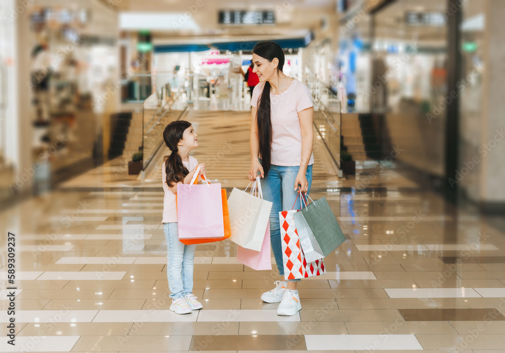 young mother and daughter holding shopping bags, shopping in the mall. Family shopping. young mother and daughter holding shopping bags, shopping in the mall. Family shopping.