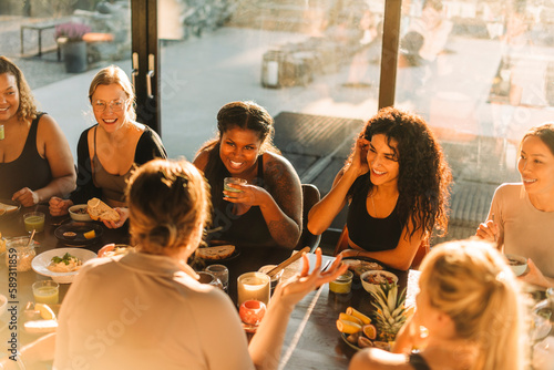 Multiracial female friends talking to each other while having breakfast at retreat center