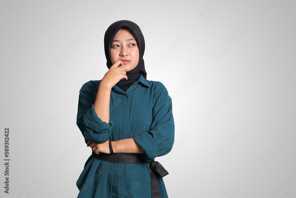 Portrait of confused Asian muslim woman with hijab standing against white background, looking up and thinking about question with hand on chin Portrait of confused Asian muslim woman with hijab standing against white background, looking up and thinking about question with hand on chin