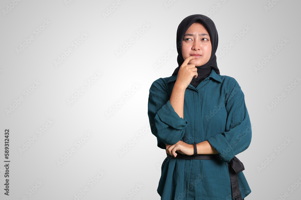 Portrait of confused Asian muslim woman with hijab standing against white background, looking up and thinking about question with hand on chin Portrait of confused Asian muslim woman with hijab standing against white background, looking up and thinking about question with hand on chin