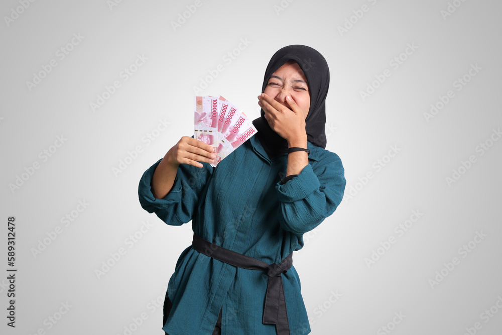 Portrait of excited Asian hijab woman in casual outfit showing one hundred thousand rupiah. Financial and savings concept. Isolated image on white background Portrait of excited Asian hijab woman in casual outfit showing one hundred thousand rupiah. Financial and savings concept. Isolated image on white background
