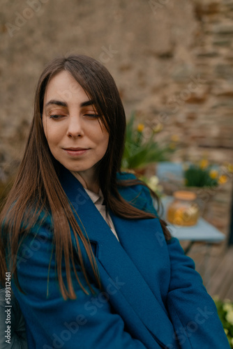 Close up outdoor photo of brunette lady with lovely smile looking down, smiling and resting on terrace near the house. 