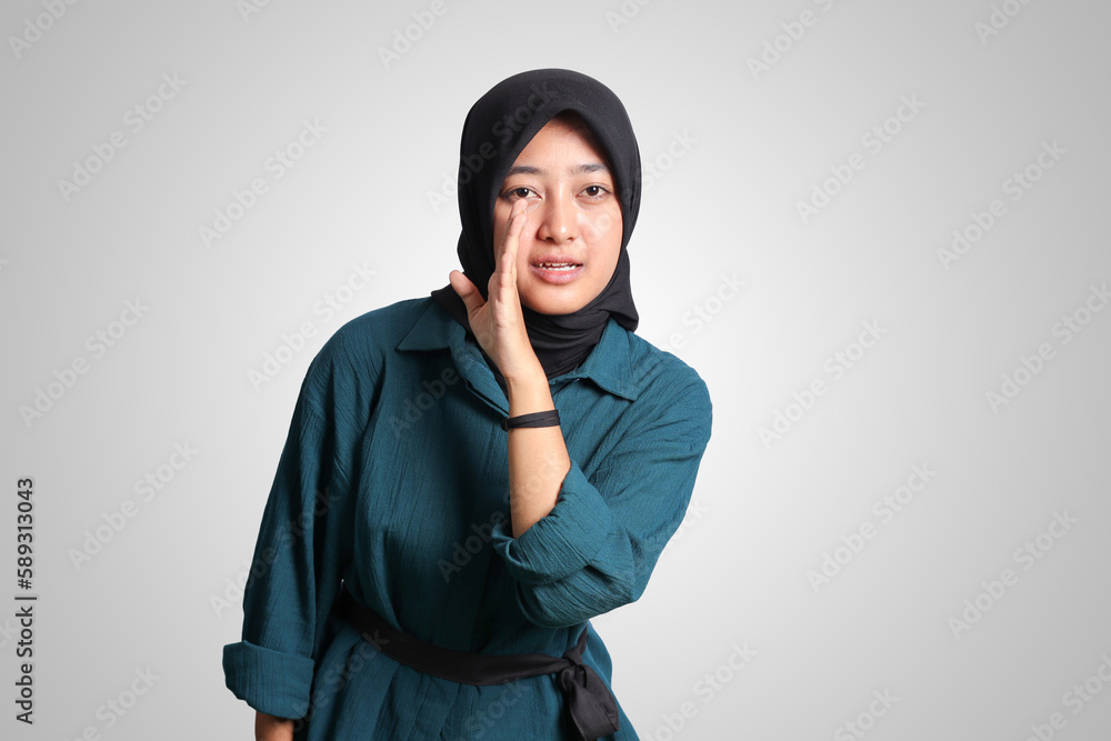 Portrait of cheerful Asian woman with hijab, trying to hear gossip or sound, holding hand near ear and listening carefully. Advertising concept. Isolated image on white background Portrait of cheerful Asian woman with hijab, trying to hear gossip or sound, holding hand near ear and listening carefully. Advertising concept. Isolated image on white background