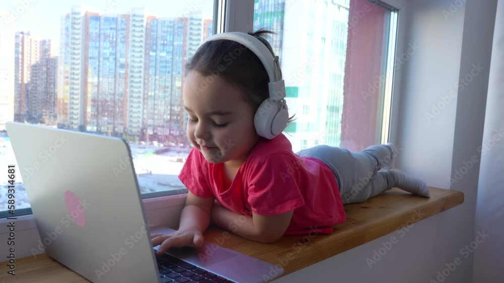 Smiling girl using a laptop, watching online lesson lying on the windowsill. Smiling girl using a laptop, watching online lesson lying on the windowsill.