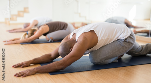 Positive man practicing yoga lesson at group class, maintaining healthy lifestyle