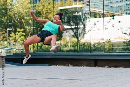 mujer morena atlética practicando patadas y saltos de capoeira en la ciudad.  photo