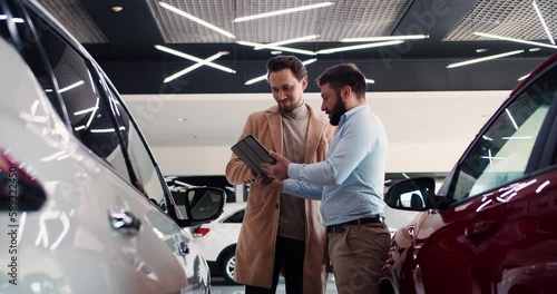 Manager of a car dealership holds tablet for signature and gives key to a happy customer