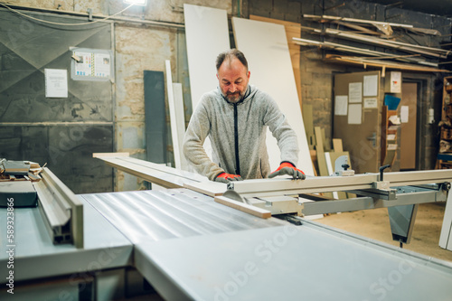 An entrepreneur is working on a saw machine at his woodshop.