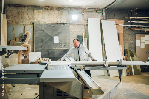 A woodworker is cutting wooden material in his workshop.