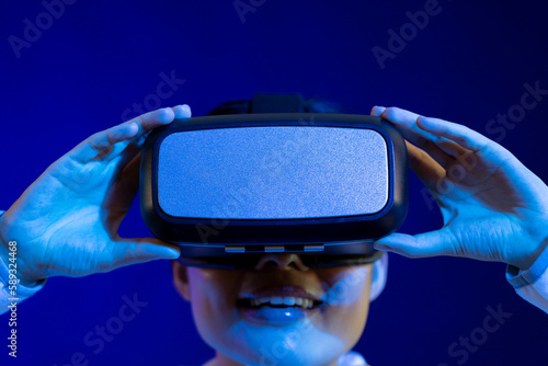 Portrait of asian woman holding vr headset in studio with blue light © vectorfusionart