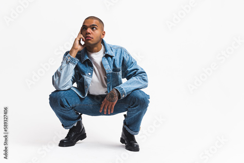 Professional fashion model in studio. Young adult male model doing a squat thinking pose over white background. Full-length studio shot. High quality photo