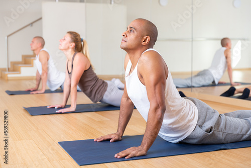 Nice people exercising during yoga class in modern fitness center